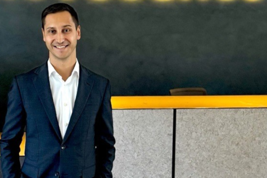 Colaborador novobanco de fato e mãos nos bolsos a sorrir com o logo logotipo por trás